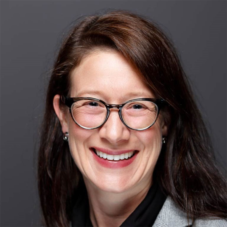 A headshot of Kimberly Geeslin, who wears a gray blazer and poses against a dark gray background.