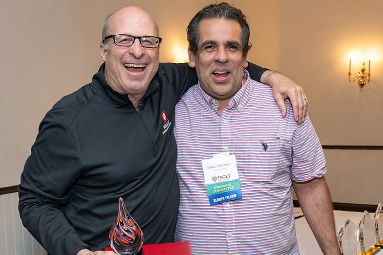 Two people smiling and posing together indoors, one holding a colorful glass award.