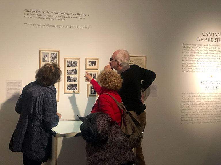 Three museum visitors viewing framed photographs and text on a wall exhibit about Federico García Lorca.